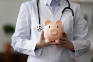 A healthcare business consultant analyzing a doctor's master fee schedule while holding a piggy bank with a stethoscope - Fee Schedule Analysis - Complete Healthcare Business Consulting