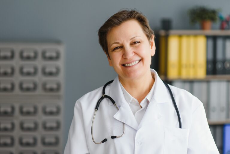 Smiling female doctor wearing a white coat and stethoscope in a medical office.