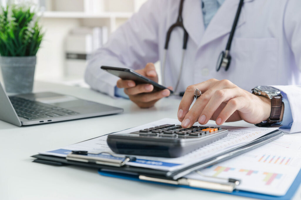 Doctor calculating medical practice finances at desk | Complete Healthcare Business Consulting