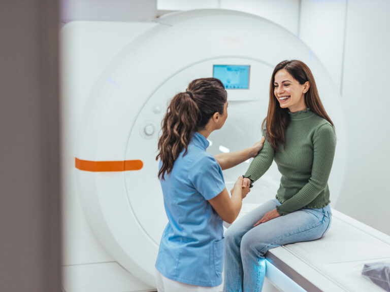 Radiology technician positioning a smiling female patient for an MRI scan in a modern imaging room.